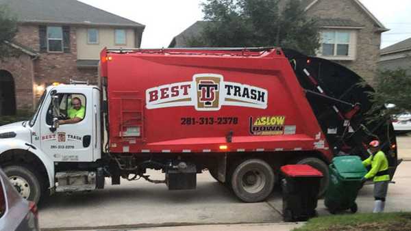 Best Trash garbage truck collecting residential waste in a neighborhood street, with sanitation workers servicing curbside trash carts in front of suburban homes.